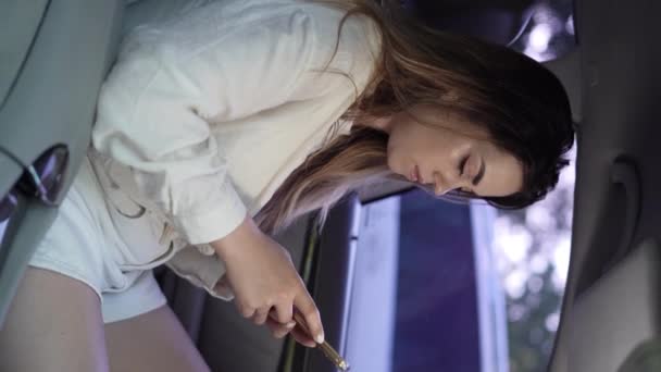 車の車輪の後ろに座っている若い女性の運転手は スマートフォンを使用して車を起動し 場所を残します バーティカルビデオ — ストック動画