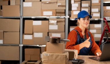 Depo çalışanı ya da müdürü iş yerindeki kameraya başparmaklarını gösterip gülümsüyor. Profesyonel fabrika işçisi kavramı. Boşluğu kopyala