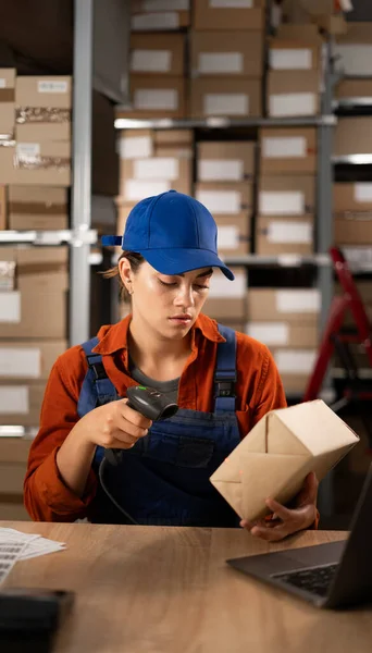 Female worker in warehouse using bar code scanner to scanning box sitting at the table. Working at warehouse. Export business concept. Copy space