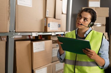 Bir depo çalışanı eşyaları bir envanter listesiyle karşılaştırıyor. Bir lojistik müdürü, bir dağıtım merkezinde depo yönetim sistemini kullanarak envanter çıkarır..