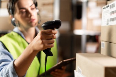 Lojistik deposunda dijital tablet kullanan bir kadın işçi. Rafların arka planında karton kutularla barkodu tarayıcı ile tarıyor. seçici odak
