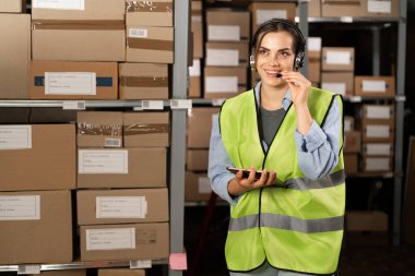 Lojistik deposundaki Brezilyalı bir kadın rafların arasında kulaklık kullanarak bir operatörle konuşuyor. Boşluğu kopyala.