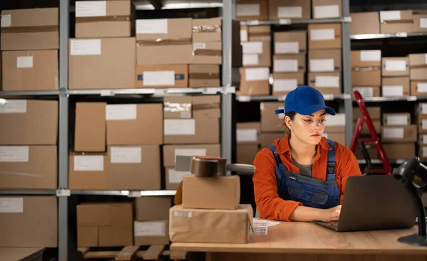 Young female worker working with laptop computer in storage warehouse. People, warehouse and industry concept. Copy space