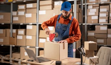 Depoda çalışan erkek işçi kargo ekommerce kutusu paketliyor web sitesinin perakende siparişini kontrol ediyor teslimat paketini masaya hazırlıyor. Boşluğu kopyala