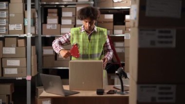 Depoda kaset kullanarak karton kutu paketleyen küçük bir iş adamı. Boşluğu kopyala