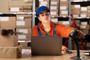 Genç bayan işçi dizüstü bilgisayarla çalışıyor ve depoda barkod tarayıcı kullanıyor. İnsanlar, depo ve endüstri konsepti. Boşluğu kopyala