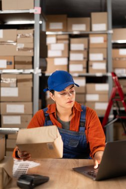 Çevrimiçi mağaza yöneticisi dizüstü bilgisayar kullanıyor, posta ücreti için bir paket hazırlıyor. Küçük işletme sahibi depoda çalışıyor, alıcı siparişi hazırlıyor. Boşluğu kopyala