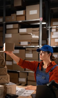 Küçük işletme girişimcisi genç bir kadın, çevrimiçi mağaza sahibi, posta kutusundaki paketleme ürünlerine teslimat paketini etiketliyor. Boşluğu kopyala.