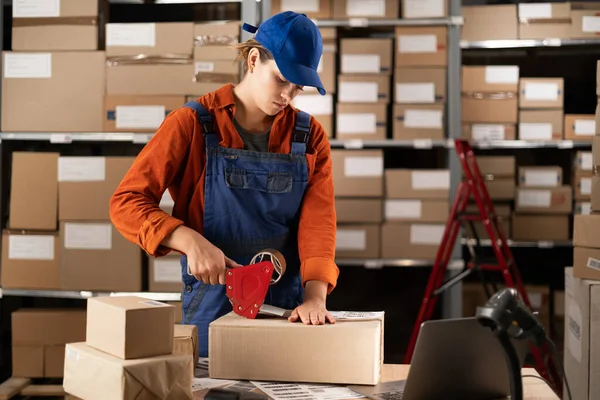 女工人在仓库里用带枪托的纸板箱包装 女雇员在大型工业仓库中包装货物 复制空间 — 图库照片