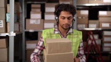Erkek işçi kulaklık takıyor. Deponun içinde kutular taşıyor. Kopya alanı.