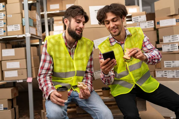 Dois Funcionários Armazém Almoçando Conversando Assistindo Algo Tela Smartphone Online — Fotografia de Stock