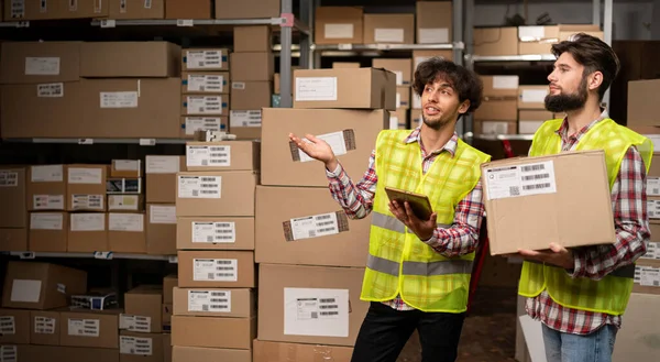 快乐的男性厂长在仓库里使用数码平板电脑 而站在货箱旁边和拿包裹的工人面前 复制空间 — 图库照片