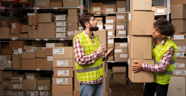 Two warehouse mixed race workers using a digital tablet while recording inventory and preparing shipment. Logistics employees working with warehouse management software in distribution center. Banner