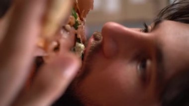 Lezzetli pizza. Genç adam iş yerinde ağzı açık bir şekilde lezzetli pizza yemekten hoşlanıyor, yakın plan. Beslenme ve fast food konsepti. Dikey video