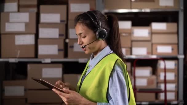 デジタルタブレットを使用して通信する物流物流倉庫で働くヘッドセットを着用する女性労働者 コピースペース — ストック動画
