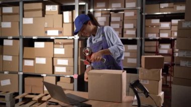 Depo çalışanı kadın, büyük bir depoda nakliye için karton kutuları yapıştırıcı bandıyla mühürlüyor. Boşluğu kopyala