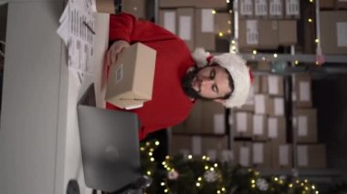 Çevrimiçi erkek satıcı elinde tarayıcı taraması yapan barkod etiketli bir posta kutusunu Noel tatilinde depoda siparişlerle birlikte paketliyor. Dikey video