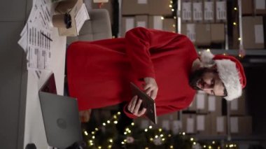 Noel Baba şapkası takan beyaz sakallı adam ve depoda çalışan kırmızı kazak sahibi. Noel hediyesi alışverişi konsepti. Teslimat için kutular. Dikey video