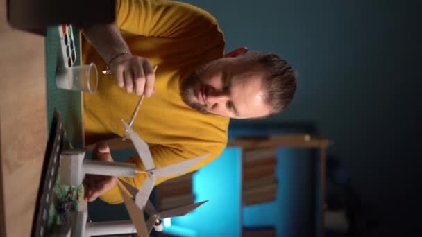 家庭のクリエイティブスタジオで風力タービンの新しい代替エネルギー開発絵画モデルに取り組んでいるひげ付き男 バーティカルビデオ — ストック動画