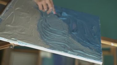 Yapısal boya kullanarak tuvali palet bıçağıyla boyayan kadın ressam kalın vuruşlar yapıyor. Dikey video