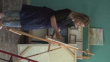 Yetenekli kadın sanatçı, yaratıcılık için palet bıçağı ve tuval kullanarak stüdyoda resim yapıyor. Dikey video