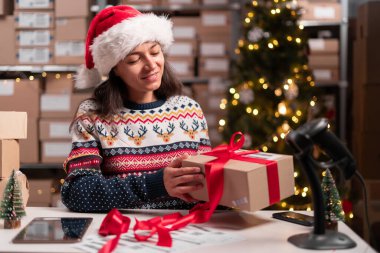 Mutlu Noel Baba 'nın elinde kırmızı kurdeleyle paketlenmiş bir hediye paketi var. Posta teslimatını ambardaki masada hazırlıyor. Mutlu Noeller nakliye konsepti. Boşluğu kopyala