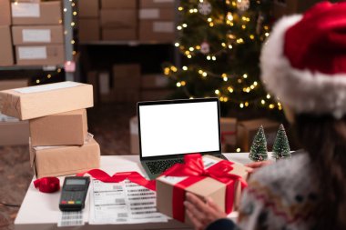 Dişi Noel Baba 'nın elinde Noel Baba hediyesi tutarken omuz hizasında boş boş dizüstü bilgisayarla e-ticaret sitesi için ekran görüntüsü oluştururken. Boşluğu kopyala