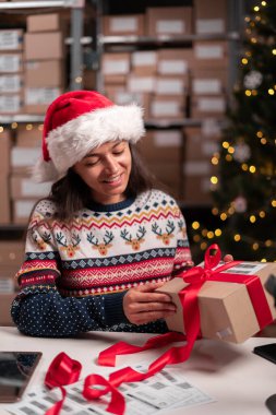 Mutlu Noel Baba 'nın elinde kırmızı kurdeleyle paketlenmiş bir hediye paketi var. Posta teslimatını ambardaki masada hazırlıyor. Mutlu Noeller nakliye konsepti. Boşluğu kopyala