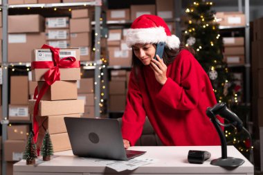 Noel Baba şapkalı satıcı, ofis çalışanları için Noel hediyeleri ve sürprizlerle dolu bir ofiste otururken cep telefonuyla sipariş alır. Küçük işletme kavramı