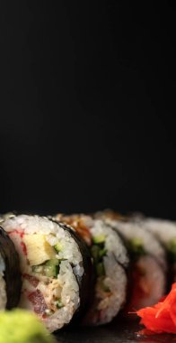 Maki Futomaki suşi rolls with ton balığı, somon, avokado, havyar ve krem peynir on black background. Dikey afiş. Boşluğu kopyala
