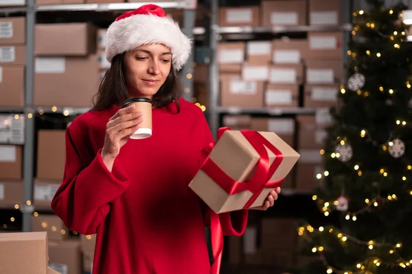 Noel arifesinde elinde karton kutuyla çalışan kadın envanter müdürü. Stok sevkiyatına hazır ürünlerle dolu paketler. Boşluğu kopyala