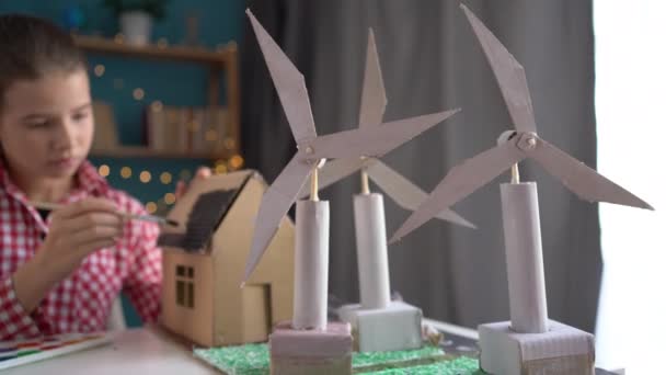 代替エネルギー源について 彼女のホームクラスで代替エネルギープロジェクトを持つ焦点と少女のテーブルに立っている風力タービン コピースペース — ストック動画
