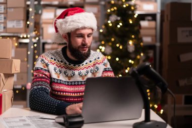 Noel teslimatı işi. Depo çalışanı depoda dizüstü bilgisayar yazılımı kullanarak paketler hazırlıyor. Sme, çevrimiçi satış kavramı