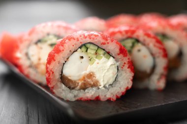 Siyah arka planda karides, masago havyarı, somon, avokado ve Philadelphia peynirli suşi rulosu.