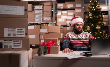Çevrimiçi mağaza müdürü Noel Baba dizüstü bilgisayar kullanıyor, yılbaşı satışında depoda çalışıyor, kendine güvenen küçük işletme sahibi müşteri siparişi hazırlıyor. Boşluğu kopyala