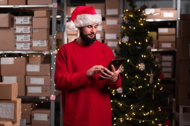 Noel zamanı çalışan erkek bir depo çalışanı. Envanter deposunda dijital tablet kullanıyor. Noel teslimatı kavramı