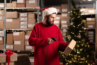 Büyük bir depoda Noel Baba şapkası tarama kutusu takan bir depo işçisi. Mutlu Noeller nakliye konsepti. Boşluğu kopyala