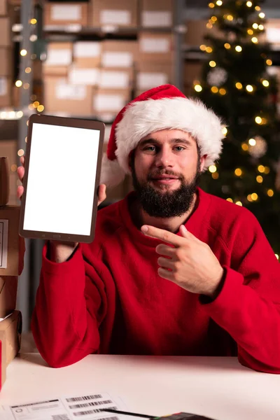 空白のタブレットコンピュータを保持するマネージャーの肖像画 サンタは荷物の準備ができているパッケージで倉庫の倉庫で働いています クリスマスセールスコンセプト — ストック写真