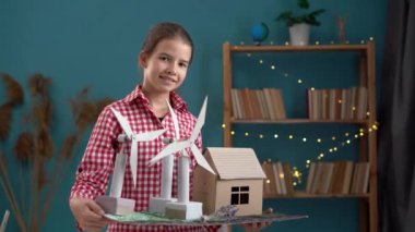 Rüzgar türbini modeli ve ev işyerindeki ev modeliyle poz veren genç bir kız. Boşluğu kopyala