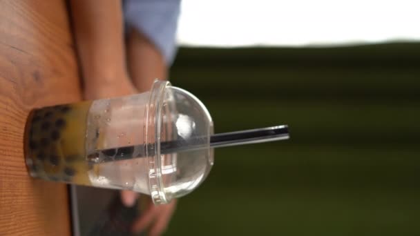 一个在咖啡馆里喝泡泡茶的女孩从桌子上拿起一个塑料杯 这是特写 垂直录像 — 图库视频影像