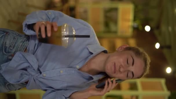 年轻的女人在餐馆里用智能手机打电话喝泡茶 垂直录像 — 图库视频影像