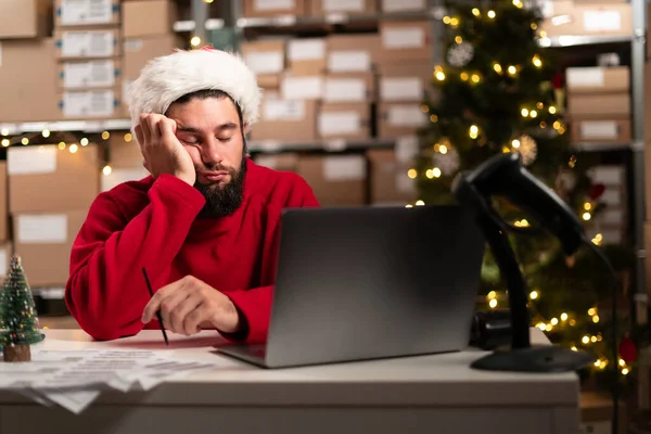 Retail warehouse employee sleeping while working at laptop computer, fatigue and overtime concept