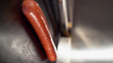 Yemek pişirme süreci. Sosisler elektrikli ızgarada kızarıyor. Fast food sosisli sandviçi için otomatik barbekü. Üst Manzara. Dikey video