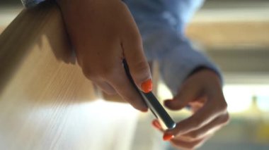 Kafeteryada otururken elinde kahve fincanı tutan ve akıllı telefona bakan genç bir kadın, yakın plan. Cep telefonu kullanan bir kız, elleri odaklı. Kahve servisi yapan bir iş kadını. Dikey video