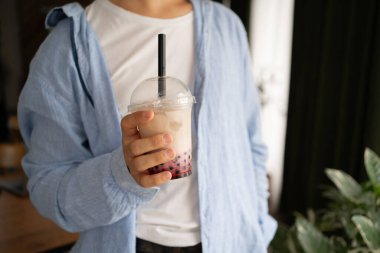 Genç adam başka yere bakar ve restoranda köpüklü çay içer. Yakın plan.