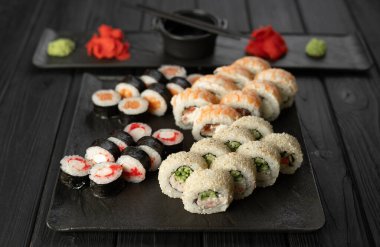 Suşi seti, siyah bir tabakta çeşitli lezzetli rulo ekmekler, ahşap bir arka plan, üst manzara. Boşluğu kopyala