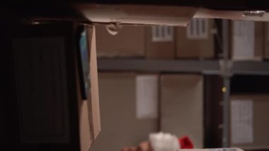 Noel Baba şapkalı bir depo işçisi raflarda kutu dolu telefon arıyor, postane arkadaşlarını arıyor. Dikey video