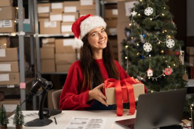 Noel masasında hediye kutularıyla bir depo çalışanı. Depoda kırmızı kurdelelerle sarılı hediyeler. Xmas Posta Teslimat Konsepti.