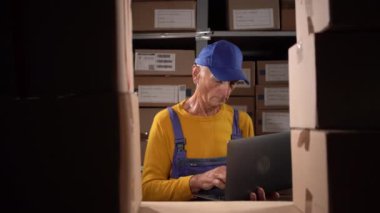 Depodaki kıdemli işadamı. Dağıtım Merkezi Yöneticisi. Karton kutuların yanındaki eski erkek yönetici dizüstü bilgisayar kullanıyor. Dizüstü bilgisayarı olan bir tatmin yöneticisi. Boşluğu kopyala