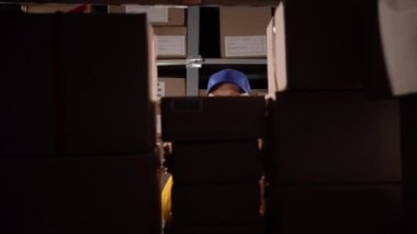 Yaşlı bir depo işçisi büyük bir depoda çalışarak raflara paketler koyuyor. Boşluğu kopyala